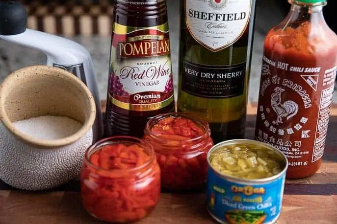 red wine vinegar, sherry, pimentos, green chilies, sriacha, pepper and salt on a wooden board