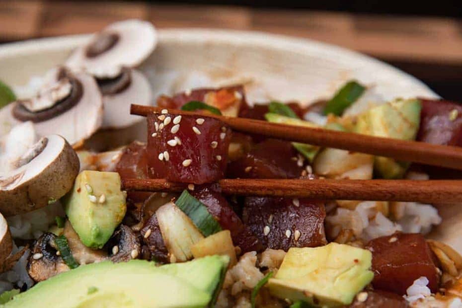 ahi tuna poke bowl with mushrooms, avocado, in a bamboo bowl with chopsticks