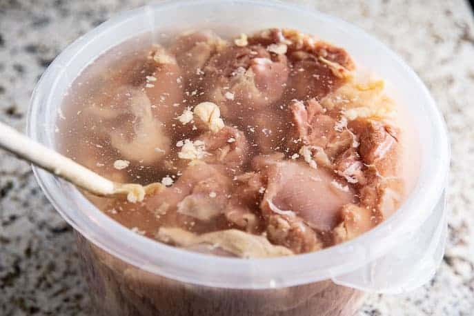 chicken thighs in plastic container of brine with wooden spoon