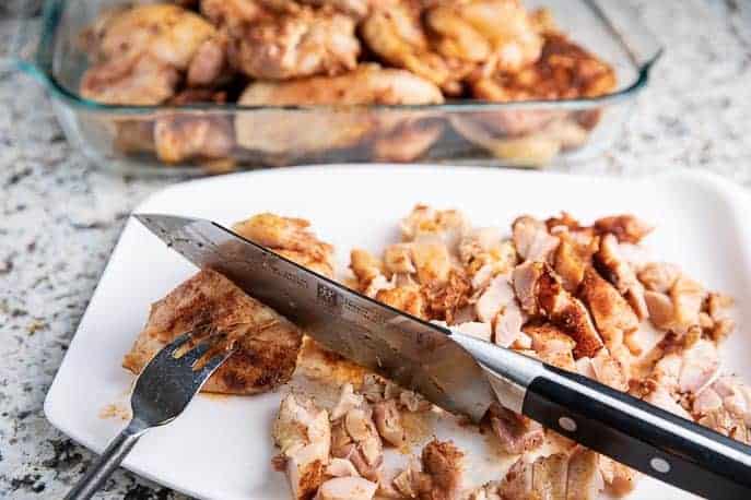 grilled chicken on a white cutting board with knife and fork, partially cut into pieces