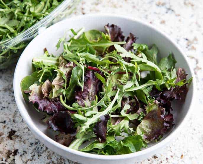 mixed greens in a white bowl on a granite counter top