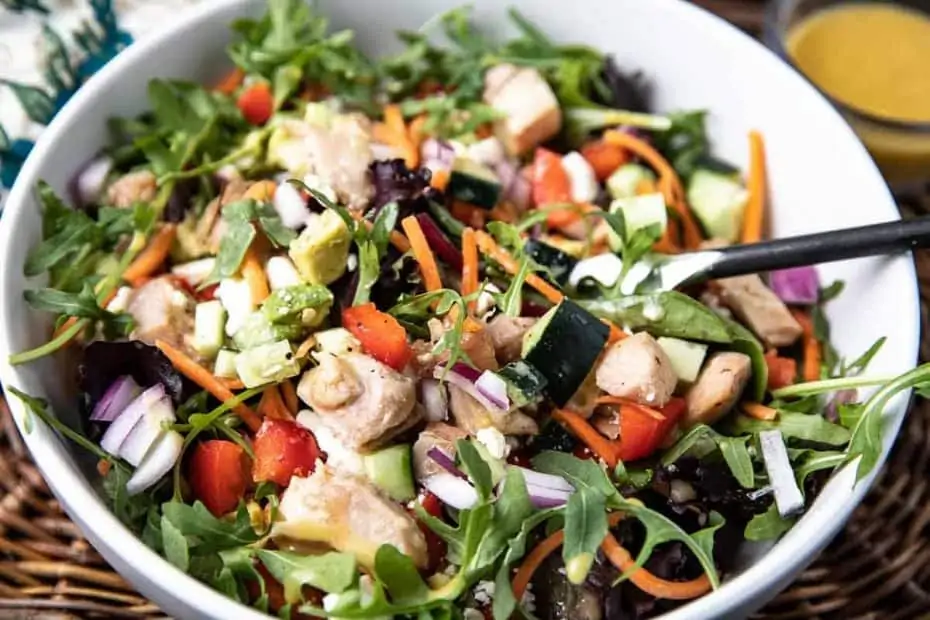 Healthy Spa Chicken Salad with Honey Mustard Dressing in a white bowl with a fork on a wicker placemat