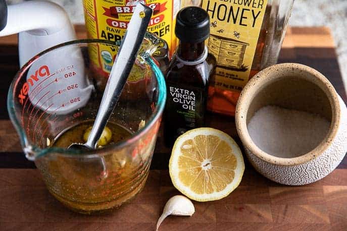 Honey Mustard Dressing ingredients - measuring cup with spoon, lemon, garlic clove, salt cellar, olive oil, honey, apple cider vinegar, pepper grinder