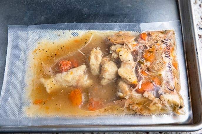 vacuum sealed bag of chicken noodle soup laying flat on baking sheet ready to freeze