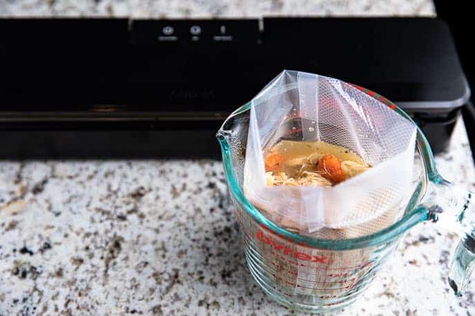 Soup in vacuum seal bag in measuring cup, vacuum sealer in background