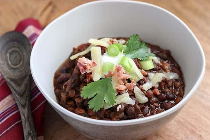 White bowl with Black Bean and Lentil Chili on a wooden board with wooden spoon and red and white napkin from Gourmet Done Skinny