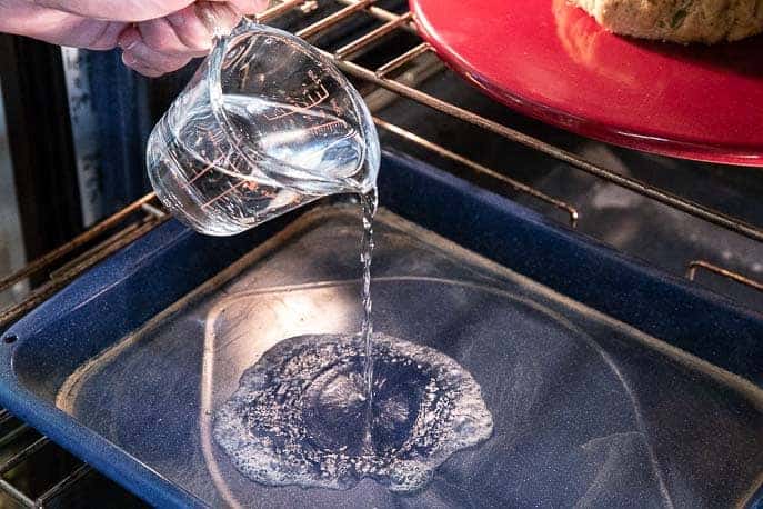 hand pouring water from measuring cup into a pan in the stove