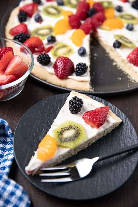 slice of fruit pizza on a black plate with pizza in background
