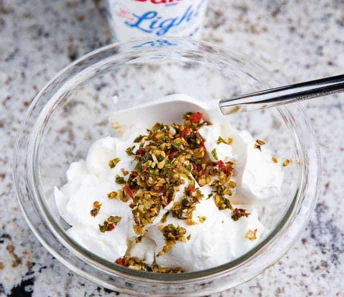 clear glass bowl with Jalapeño Cream Sauce, spatula and light sour cream container in background