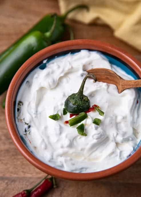 Jalapeño Cream Sauce in a pottery bowl with a wooden spoon and napkin and jalapenos and peppers on wooden board