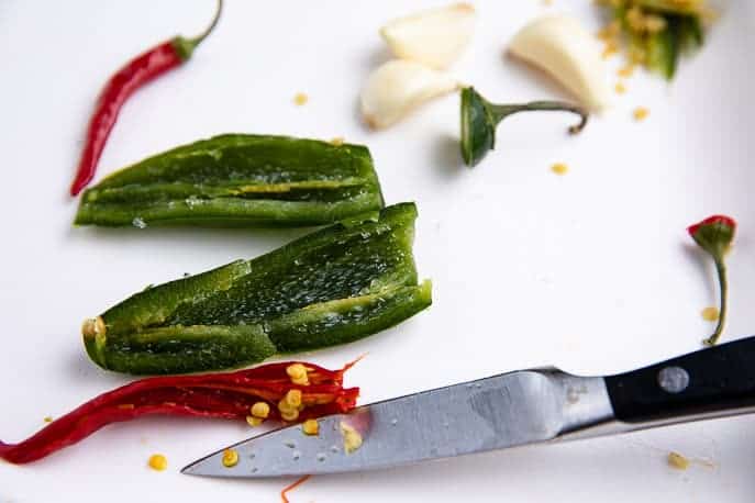 jalapeno peppers, red peppers, garlic on a cutting board with knife