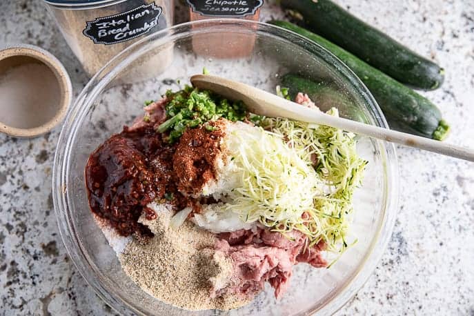 glass bowl with ingredients for turkey sliders, wooden spoon, zucchini, bread crumbs and salt on granite counter top