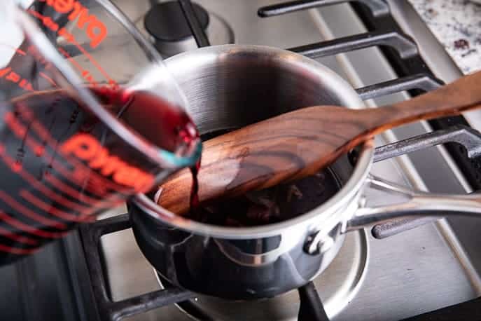 pouring wine into a saucepan with wooden utensil