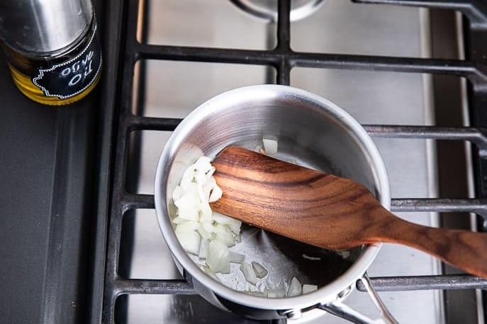 saucepan on stove with onions and wooden utensil