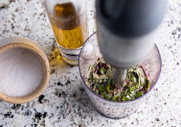 immersion blender in a cup with vinaigrette mixture, salt in cellar and bottle of olive oil