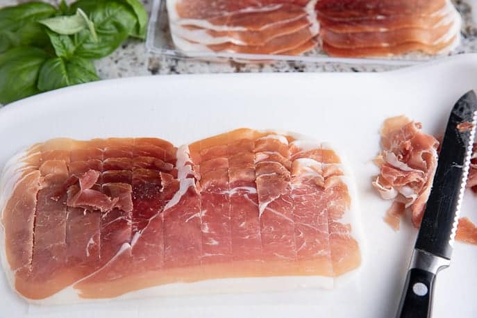 prosciutto on a white cutting board with a knife