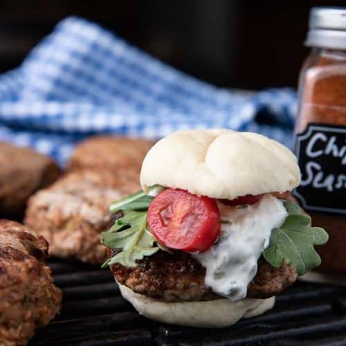 adobo turkey slider with Jalapeno cream on a slider bun with lettuce, sliders in the background, blue napkin, chipotle seasoning on a grill