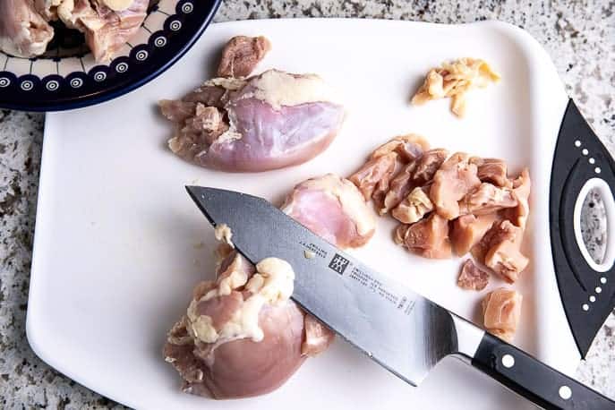 cutting board with knife, chicken and cut pieces of chicken