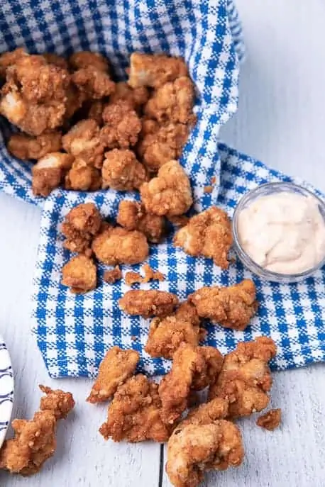 air fryer popcorn chicken on a board with sauce vertical