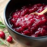 cooked cranberries in a black bowl with wooden spoon and rosemary