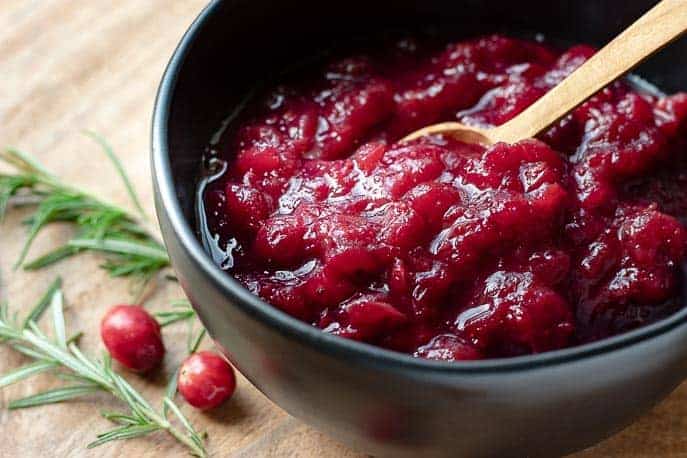 cooked cranberries in a black bowl with wooden spoon and rosemary