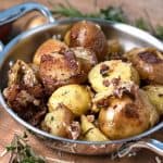 Easy Instant Pot Crispy Parmesan Potatoes in a 2 handled skillet with potatoes and herbs in the background