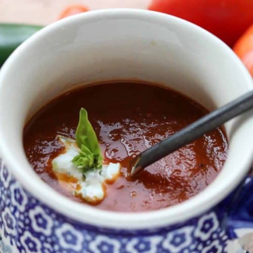 tomato soup in a cup with basil, tomatoes, jalapenos around