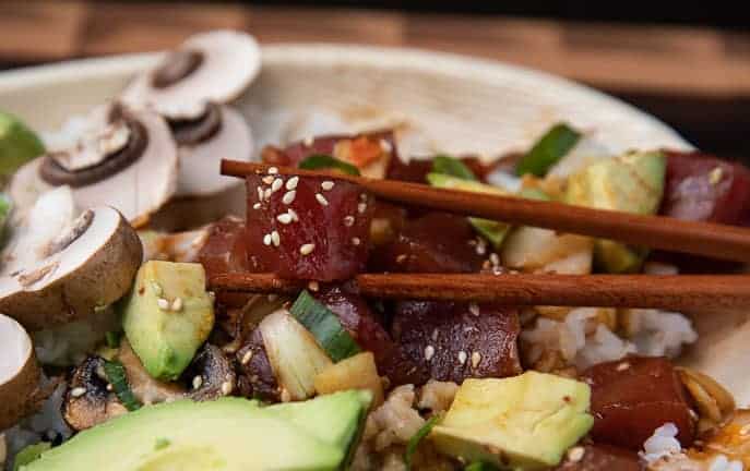 ahi tuna poke bowl with mushrooms, avocado, in a bamboo bowl with chopsticks