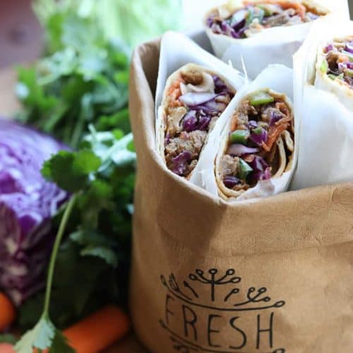 Thai wrap on a wooden board with wraps in a bag, cilantro, cabbage and carrots from Gourmet Done Skinny