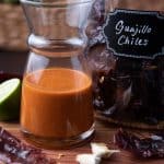Guajillo Chili Lime Vinaigrette in a glass jar with chiles, lime and garlic on a wooden board