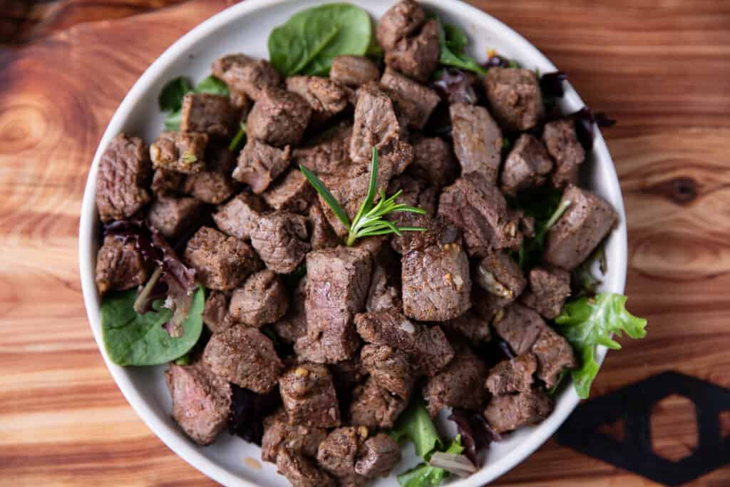 steak bites on a white plate with greens