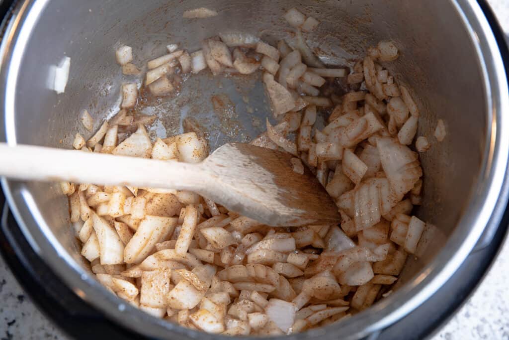 onions and spice in Instant Pot with wooden spoon