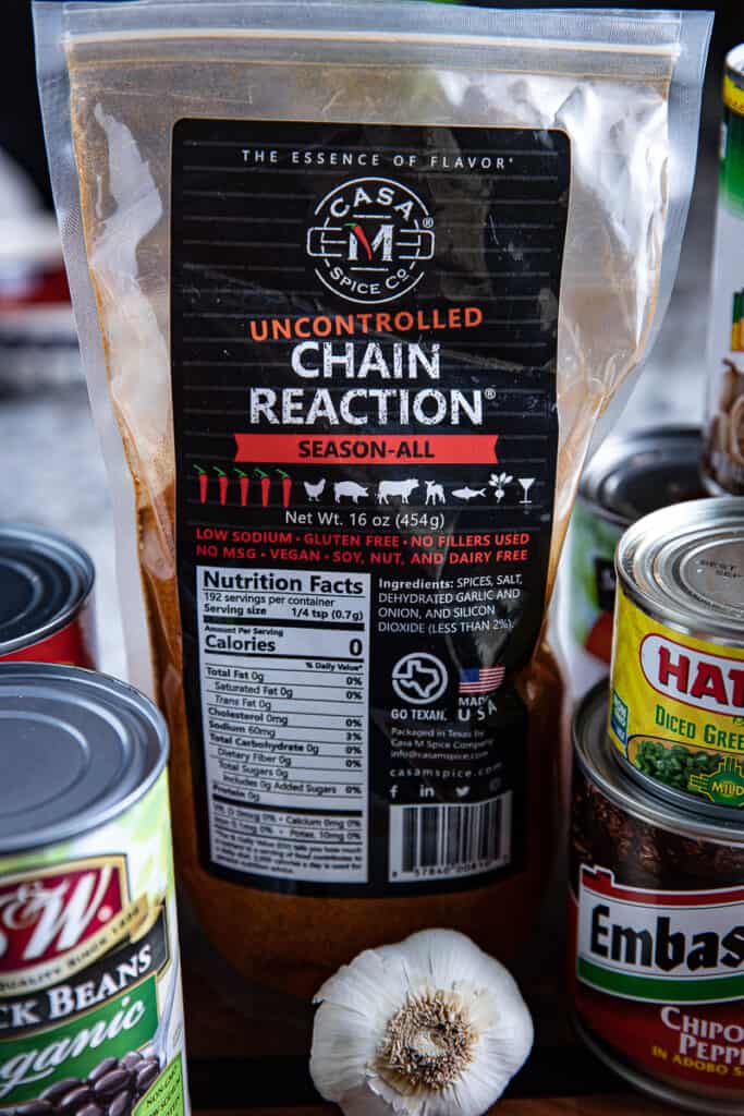 A bag of Casa M Chain Reaction Spice surrounded by canned vegetables