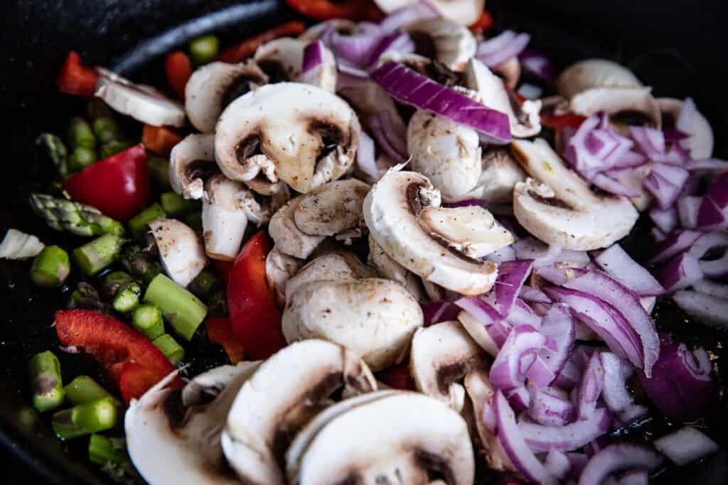mushrooms, onions, peppers, asparagus in a cast iron skillet