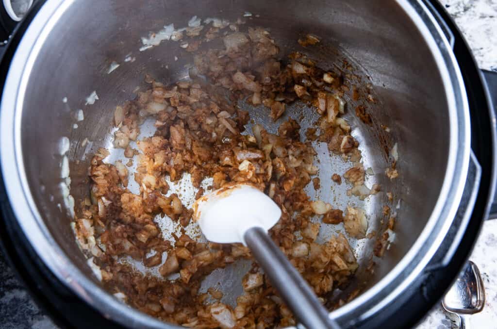 onions, spices in Instant Pot with spatula