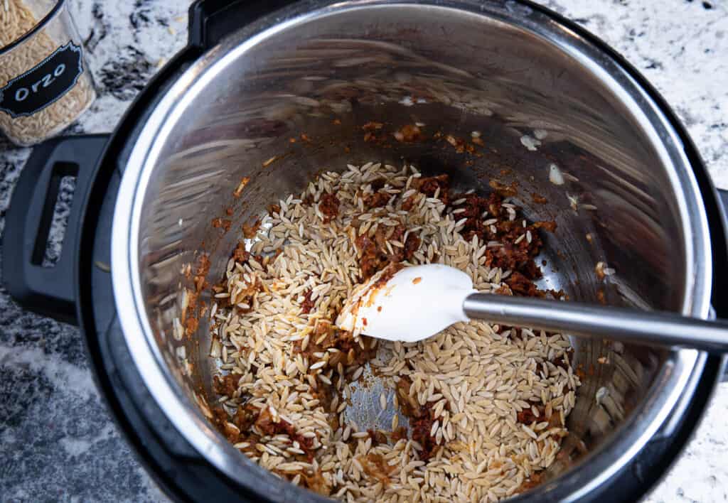 orzo, spices in Instant Pot with spatula