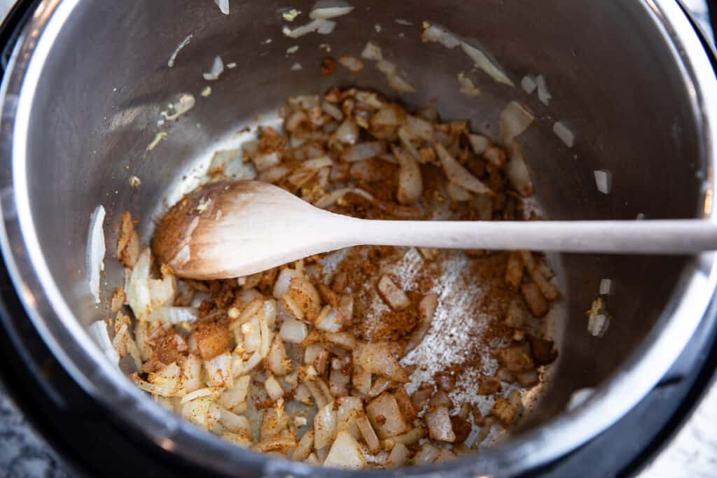 onions and spice in Instant Pot with spoon